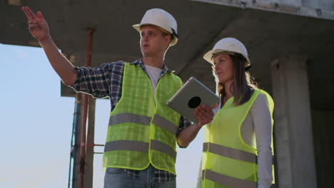 Professional-engineers-in-safety-vests-and-helmets-working-with-digital-tablet-and-blueprints